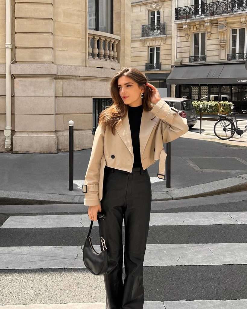 Classic spring outfit with beige cropped trench coat, black turtleneck sweater, black wide-leg trousers and black leather shoulder bag
