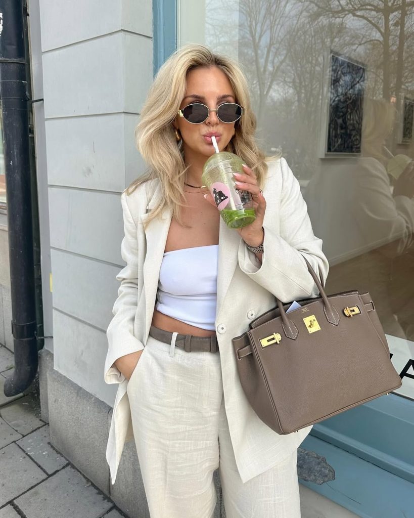 Elegant modern outfit with cream linen blazer, white bandeau top, cream linen pants, taupe belt, designer handbag and oval sunglasses