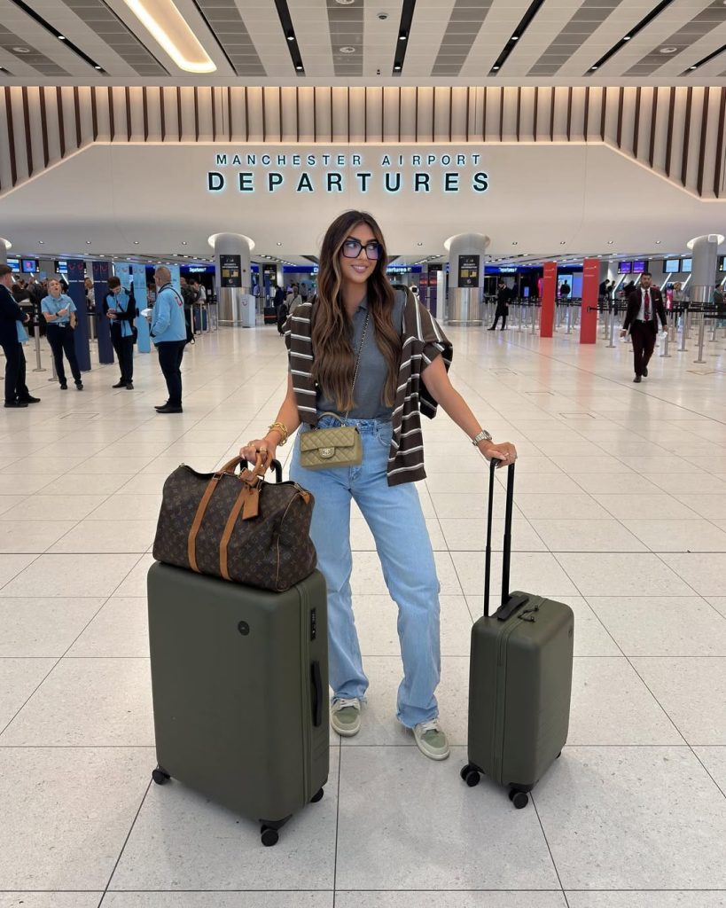 Casual airport outfit with gray t-shirt, light blue straight jeans, black and white striped sweater, designer crossbody bag and oversized blue glasses