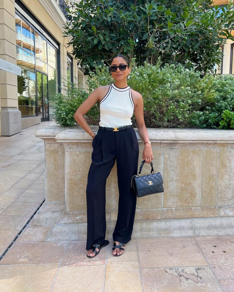 Elegant European vacation outfit with white contrast-trim halter top, black wide-leg trousers, designer gold belt, quilted luxury handbag and leather sandals