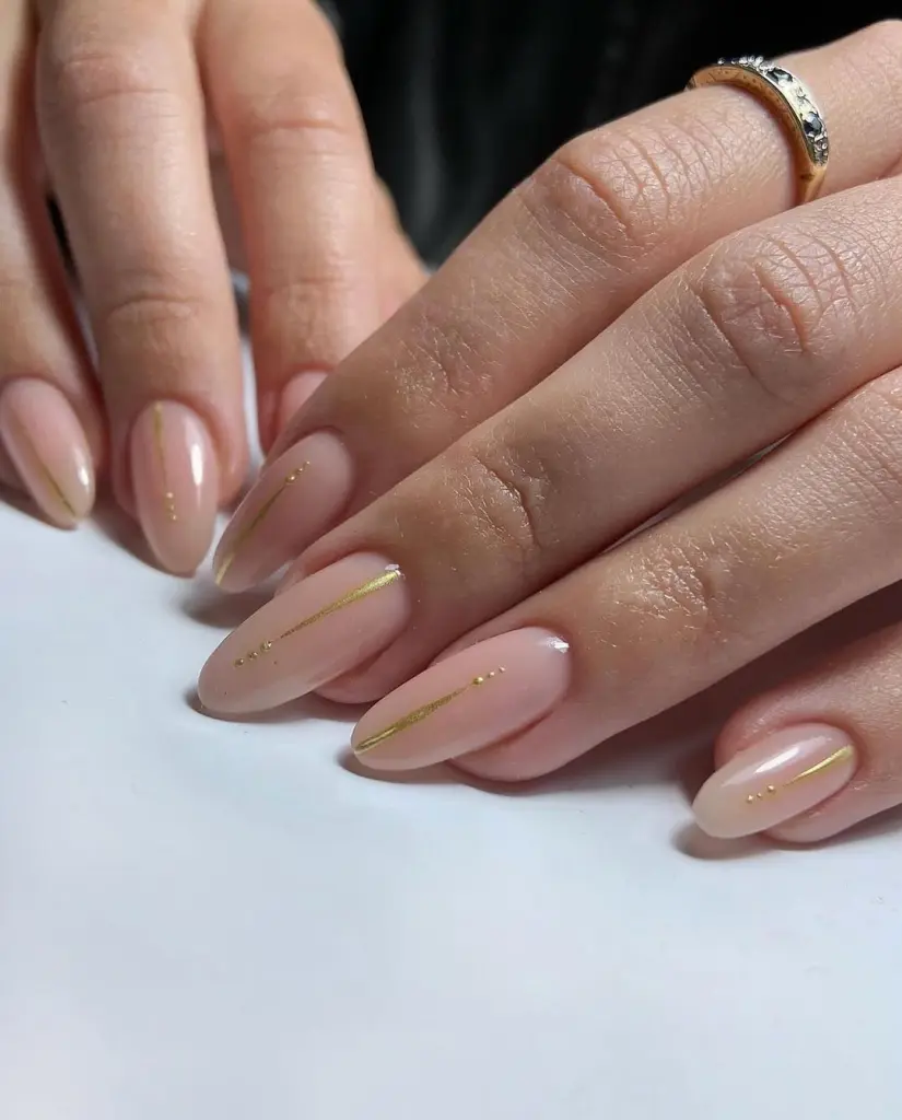 Almond-shaped minimalist nails with translucent nude base and thin gold line details