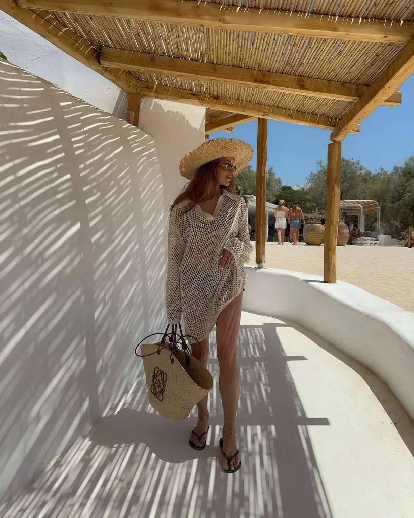 Beach vacation outfit with cream crochet loose tunic cover-up, straw wide brim hat, designer logo straw tote bag and black flip flops