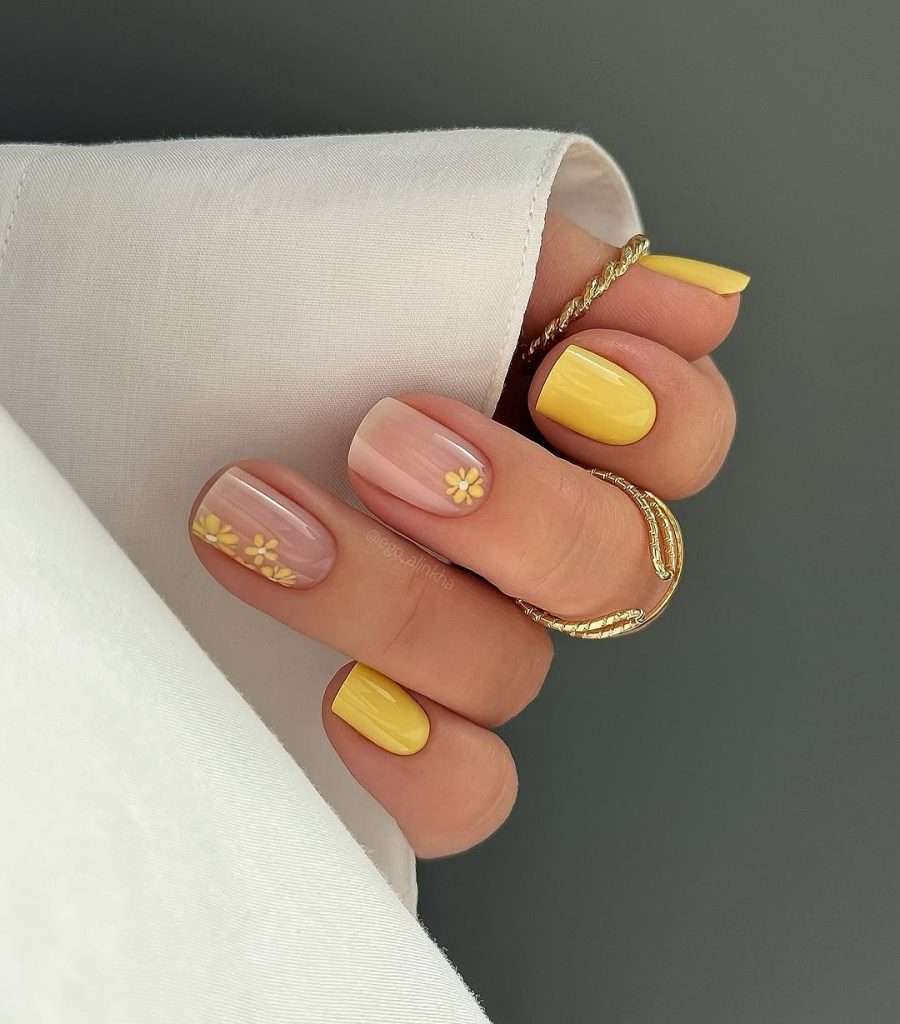 Short square nails with yellow accent nails and nude base with yellow daisy art
