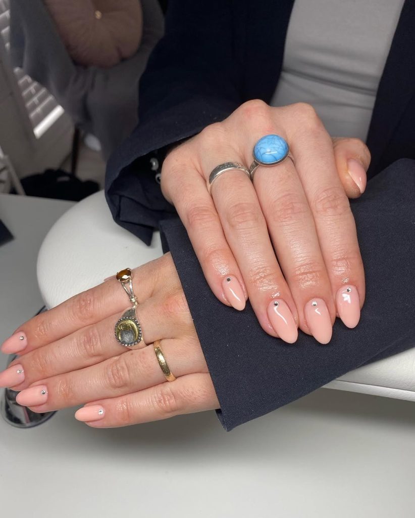 Almond shaped peach-pink nails with minimalist single crystal accent on each nail