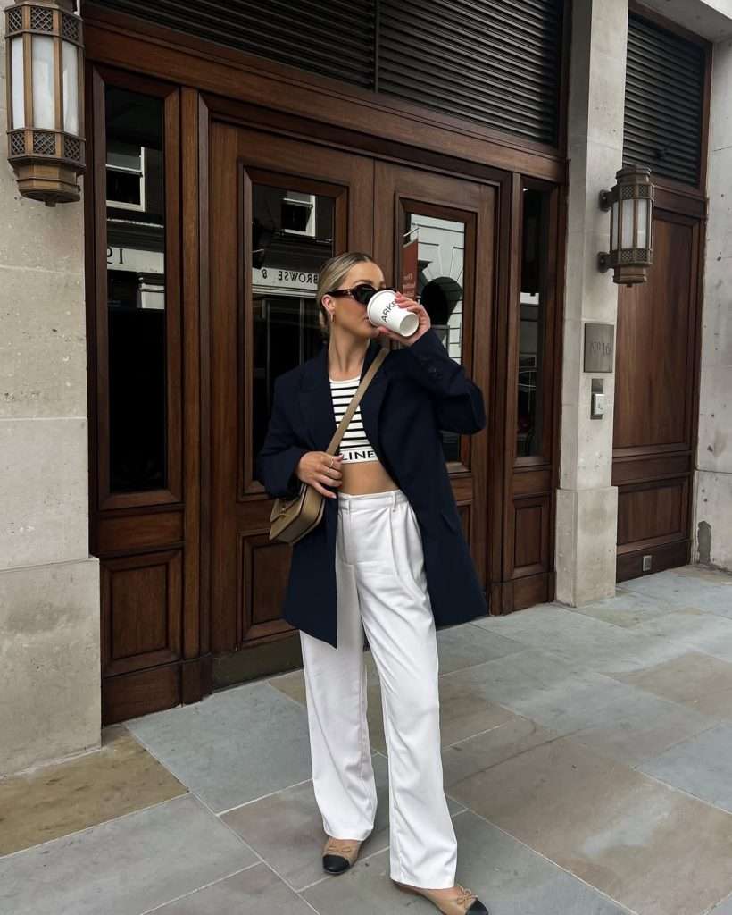 spring outfit with navy wool coat, black and white striped crop top, white wide-leg trousers, beige and black ballet flats and tan shoulder bag

