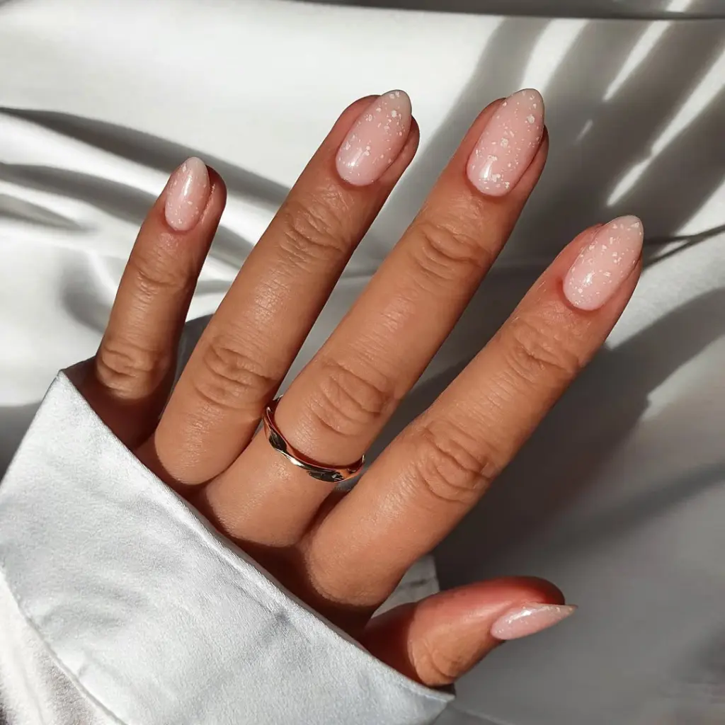 Almond-shaped minimalist nails with milky nude base and scattered white micro-dot accents