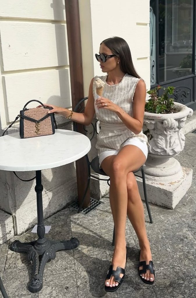 Fresh European vacation outfit with cream textured sleeveless peplum top, matching shorts, black minimal sandals and small shoulder bag
