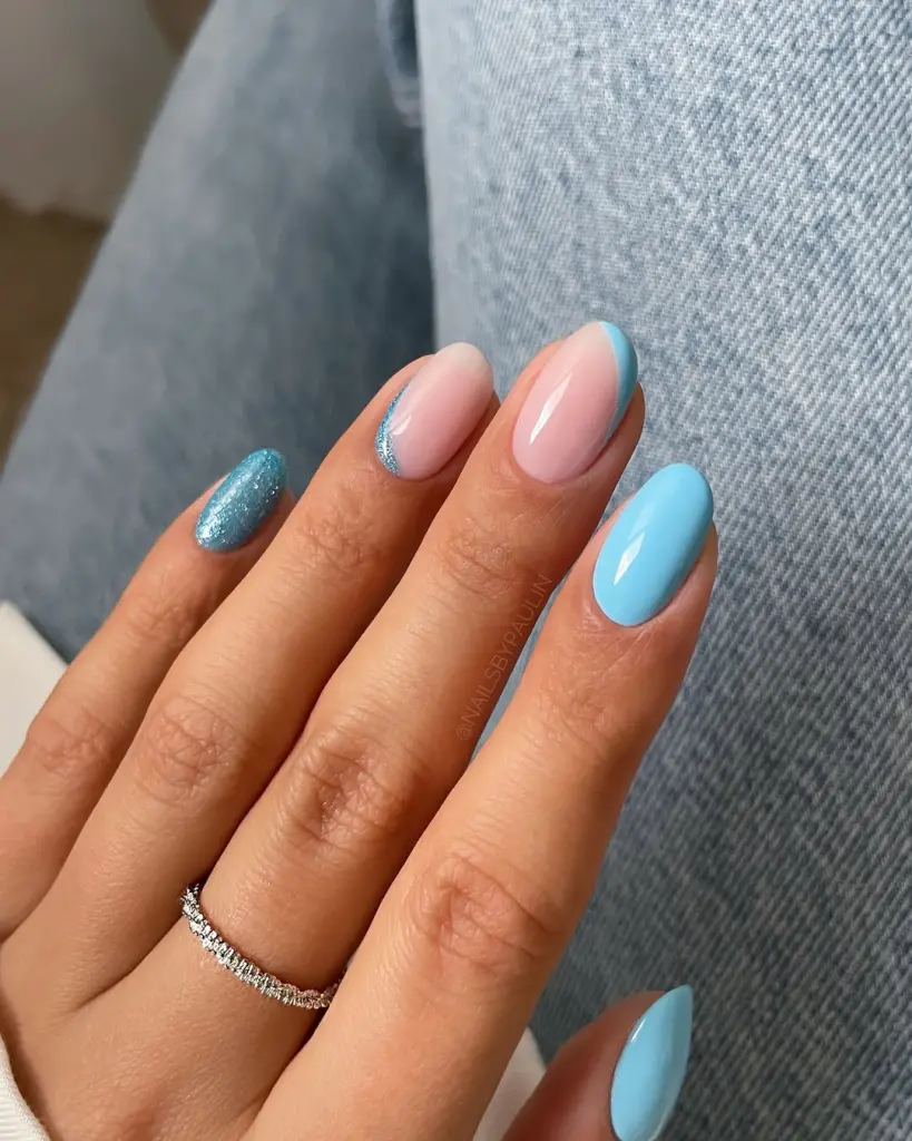 Oval summer nails with baby blue polish, aqua glitter accent nail and nude base with blue line detail
