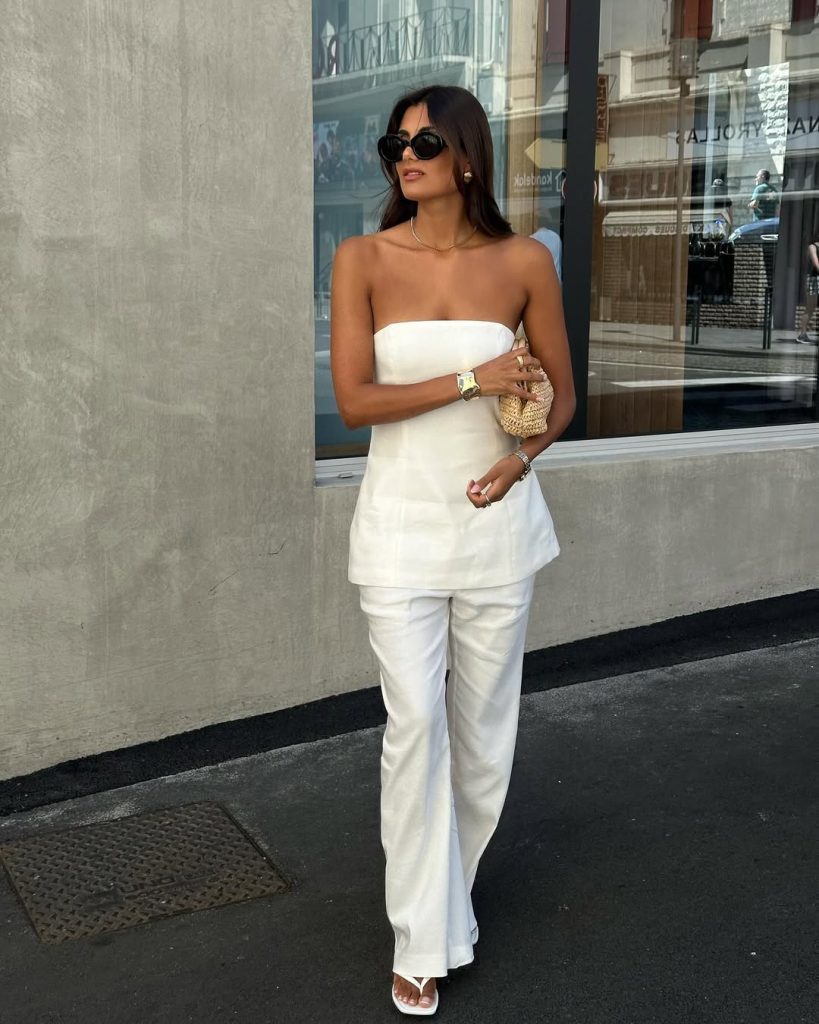 Elegant minimal outfit with white strapless tube top, white wide-leg linen pants, miniature woven clutch, gold jewelry and oversized black sunglasses

