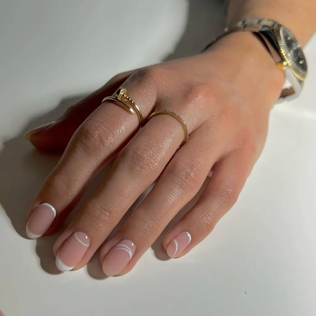 Short round minimalist nails with sheer pink base, white curved French tips and thin white curved line accents