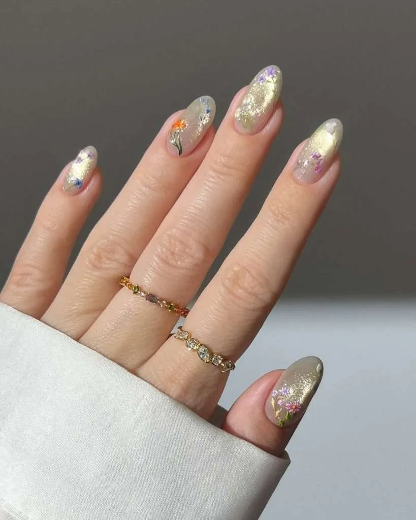 Almond shaped nails with gold shimmer tips and tiny colorful flower designs