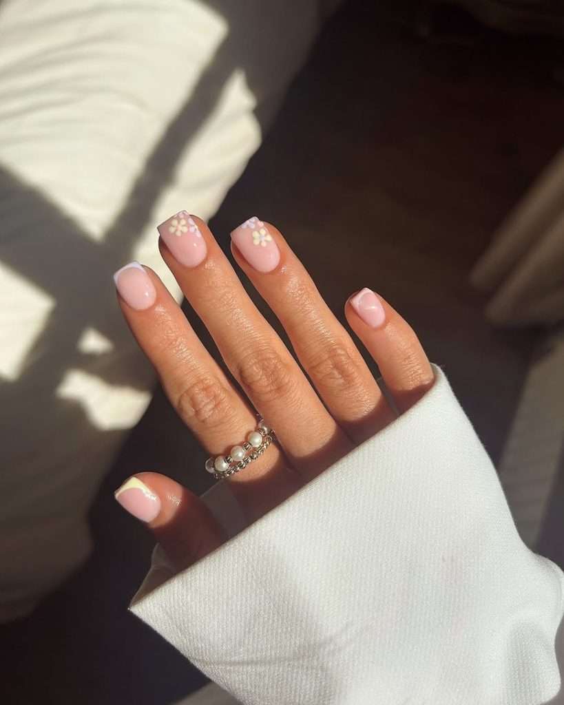 Short square pink nails with white French tips on some nails and small white daisy flower details for delicate spring manicure