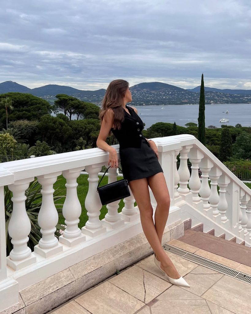 Sophisticated European vacation outfit with black sleeveless button-front vest, coordinating mini skirt and structured black clutch bag