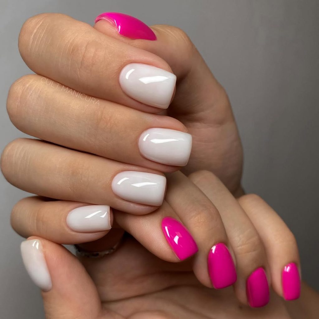 Short summer nails with glossy hot pink polish on one hand and milky white polish on the other creating a bold two-tone manicure