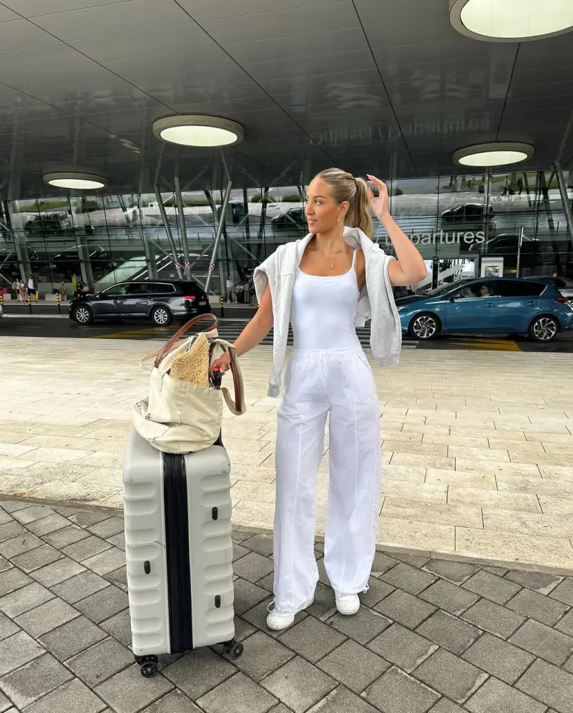 Elegant airport outfit with white tank top, white linen pants, gray draped sweater, white sneakers and beige canvas tote