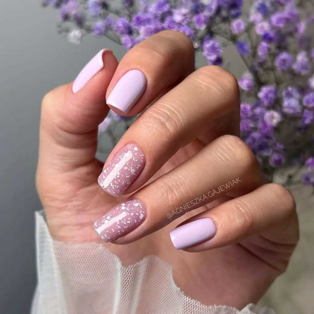 Short square elegant spring nails with alternating solid lilac and lilac base with white speckles against purple flower background