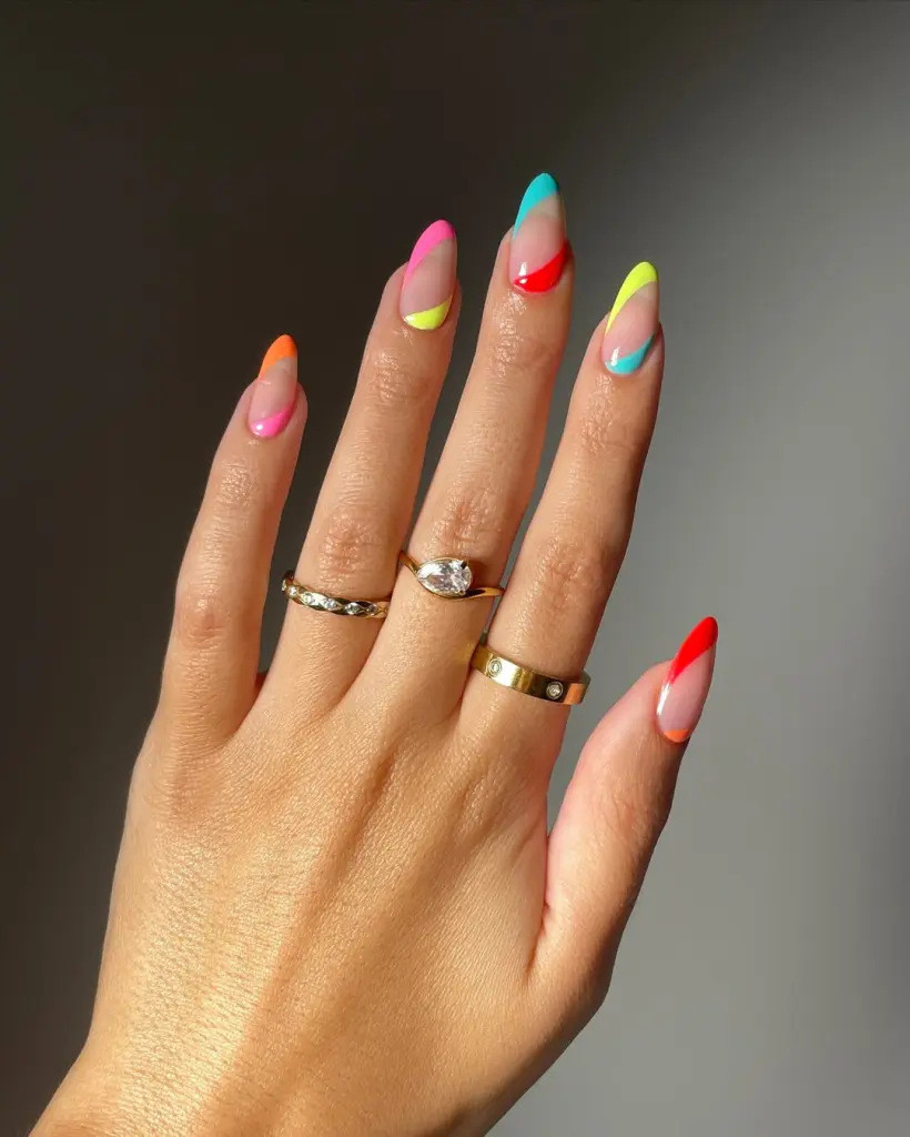 Almond shaped summer nails with sheer base and asymmetrical neon color accents in orange, pink, yellow, turquoise and red
