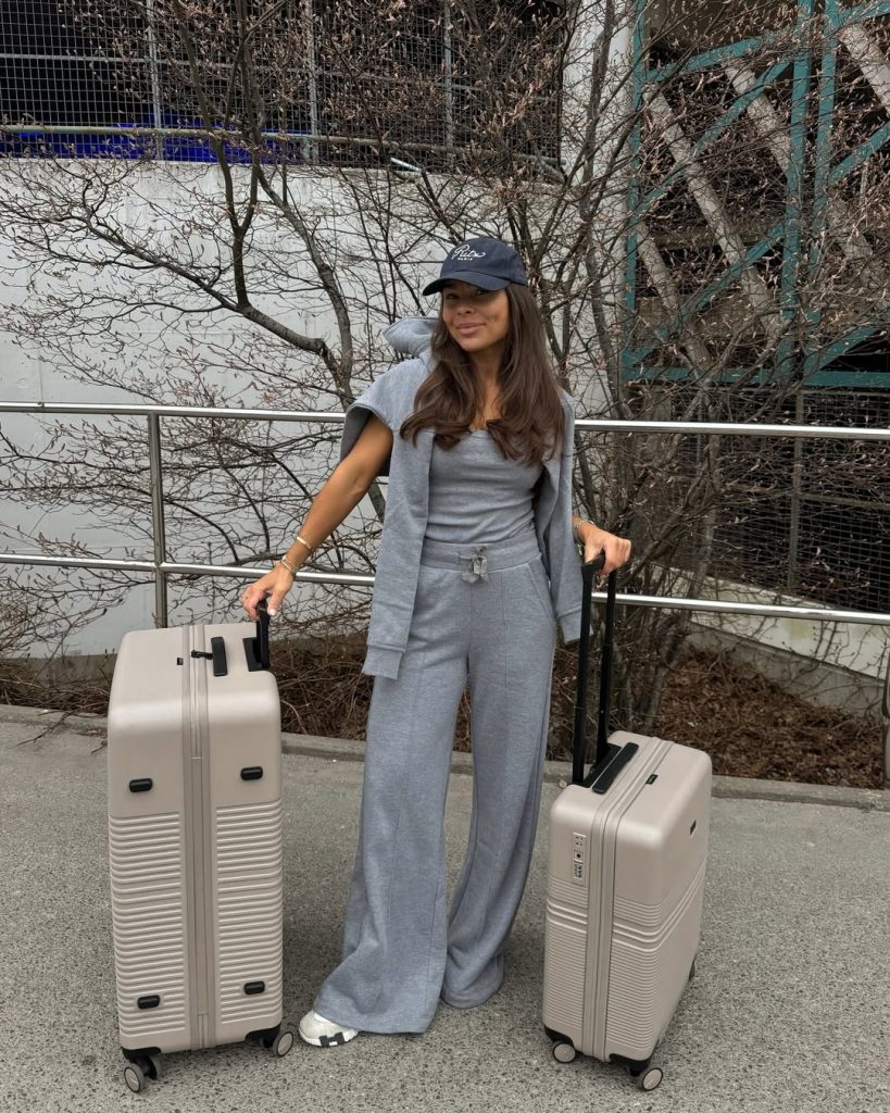 Comfortable airport outfit with gray tank top, matching wide-leg sweatpants, coordinating gray sweatshirt, navy baseball cap and white sneakers