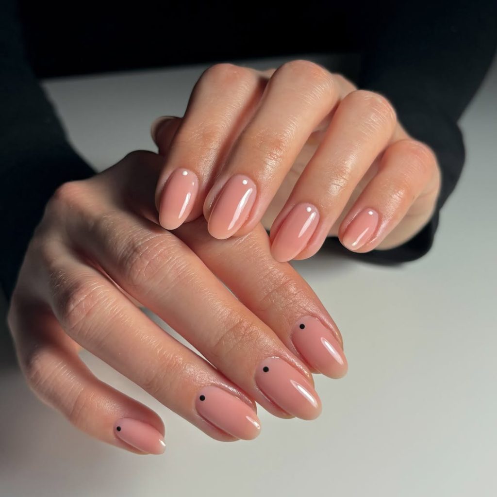 Almond-shaped minimalist nails with glossy peach base and contrasting micro dots - black dots on one hand, white dots on the other
