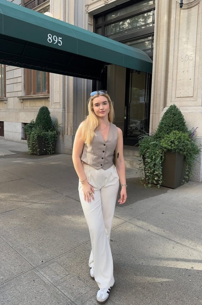 Summer business casual outfit with taupe fitted vest, white wide-leg trousers, white athletic sneakers, small chain crossbody bag and simple gold jewelry
