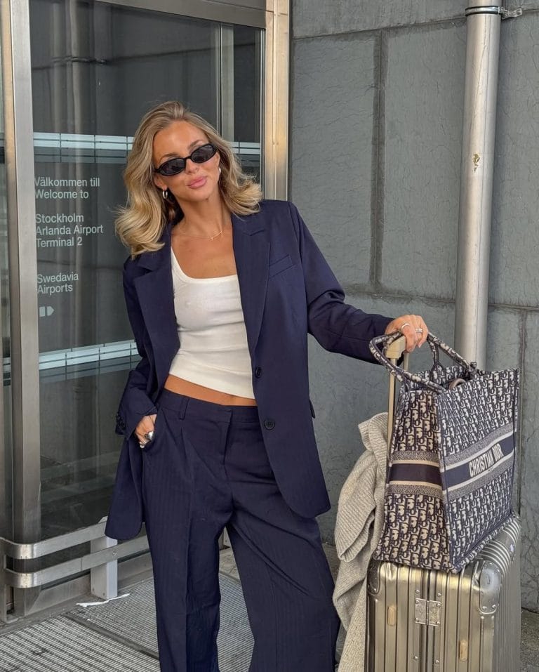 Stylish airport outfit with navy blue oversized suit, white top, metallic chunky sneakers, black sunglasses and designer tote bag