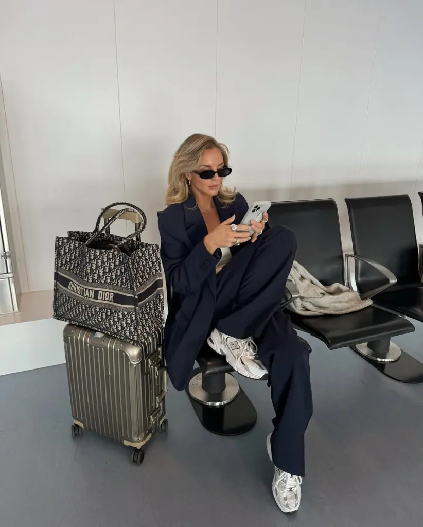 Stylish airport outfit with navy blue oversized suit, white top, metallic chunky sneakers, black sunglasses and designer tote bag