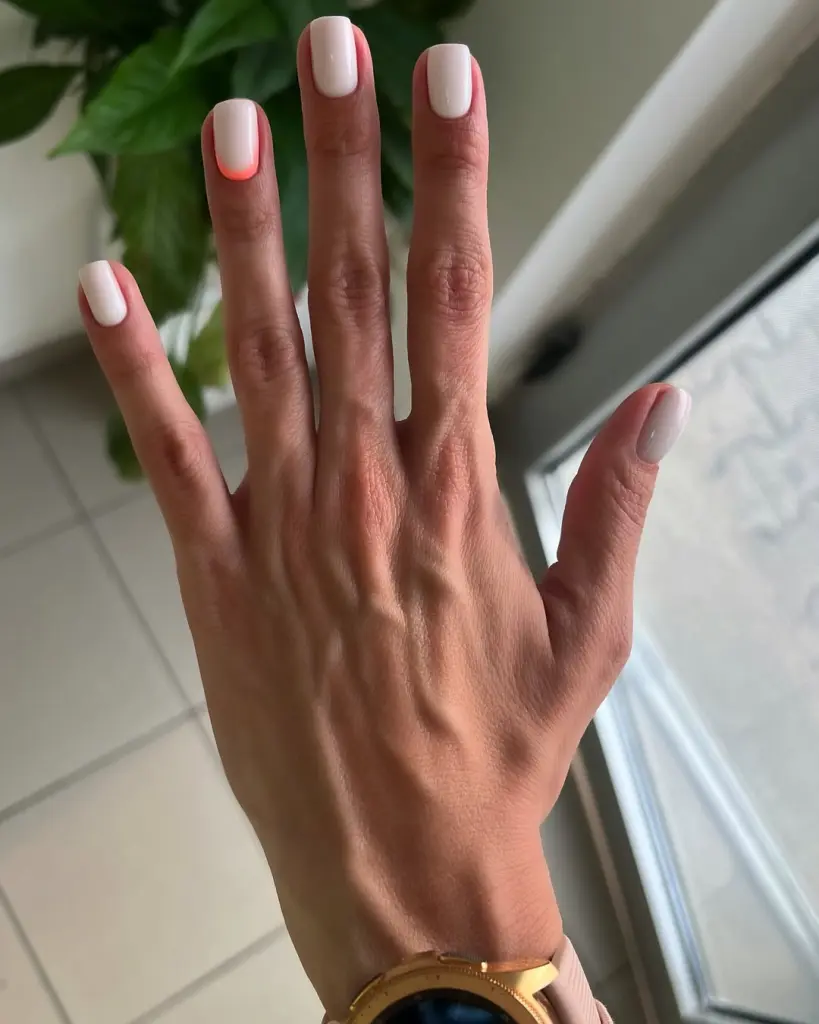 Short summer nails with uniform milky white polish featuring a subtle coral accent detail at the cuticle on one nail
