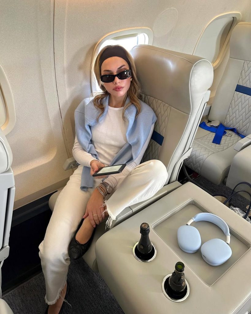 airport outfit with cream ribbed sweater, white distressed jeans, light blue cardigan, black headband, slim sunglasses and black designer flats with blue headphone