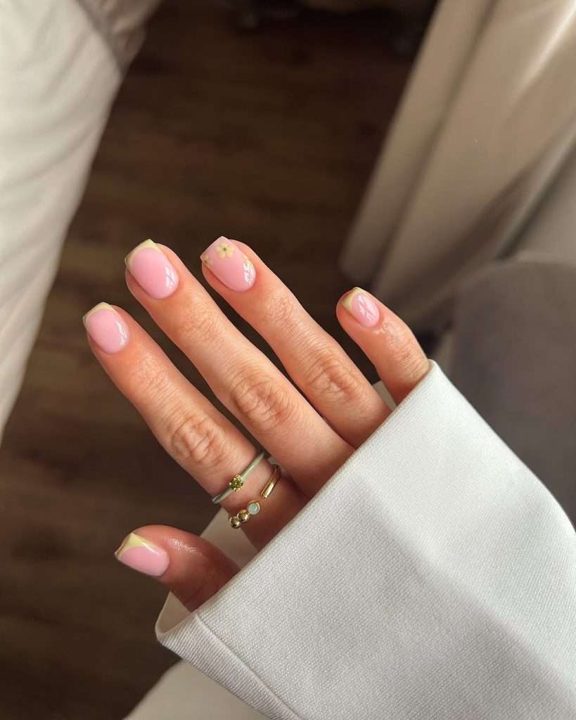 Short spring nails with pink base, sage green French tips and small floral accent design

