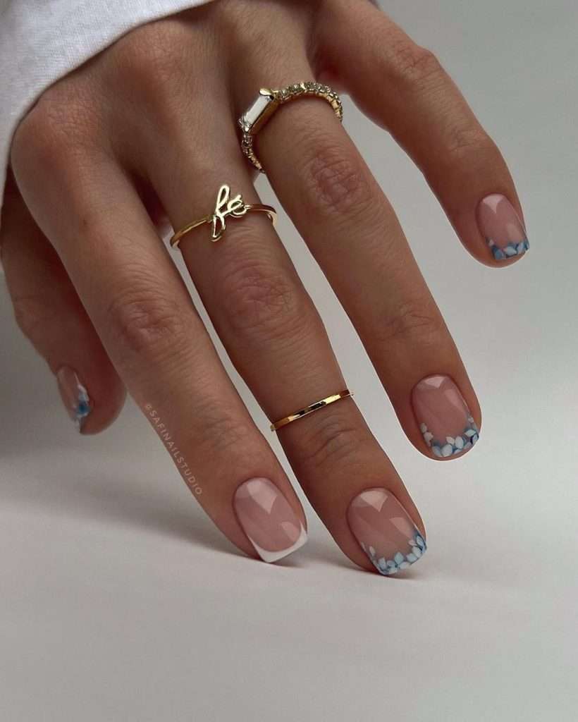 Short square nails with nude base and white French tips decorated with blue and white flower petals
