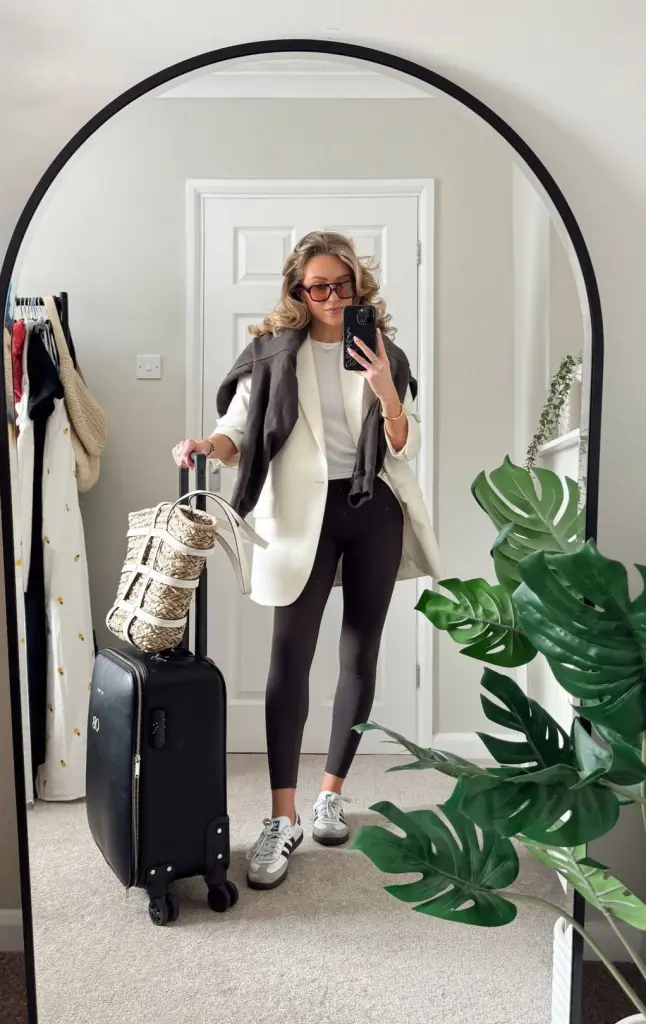 Travel outfit with white oversized blazer, white t-shirt, charcoal leggings, gray scarf, vintage-inspired sneakers, amber glasses and straw basket tote