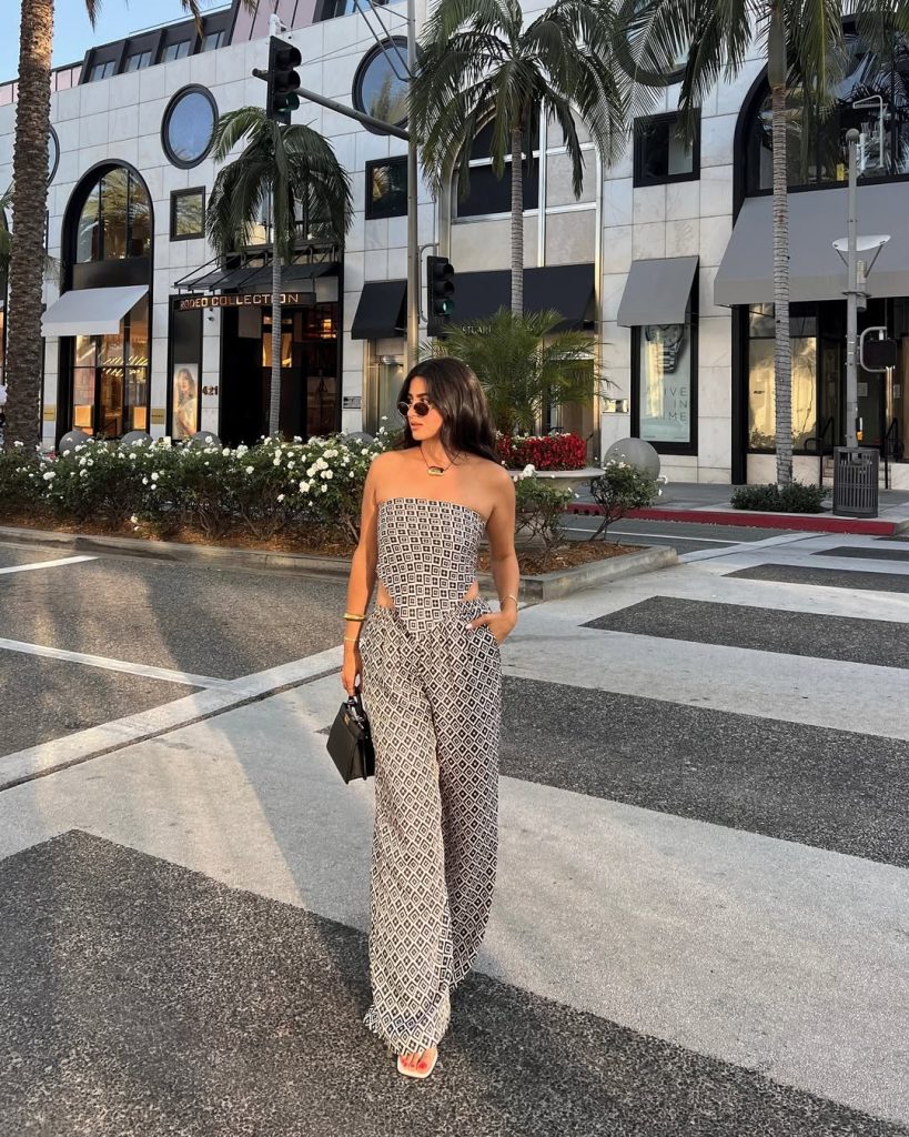Summer outfit with black and white geometric print strapless top, matching wide-leg pants, oval sunglasses, statement necklace and small black handbag

