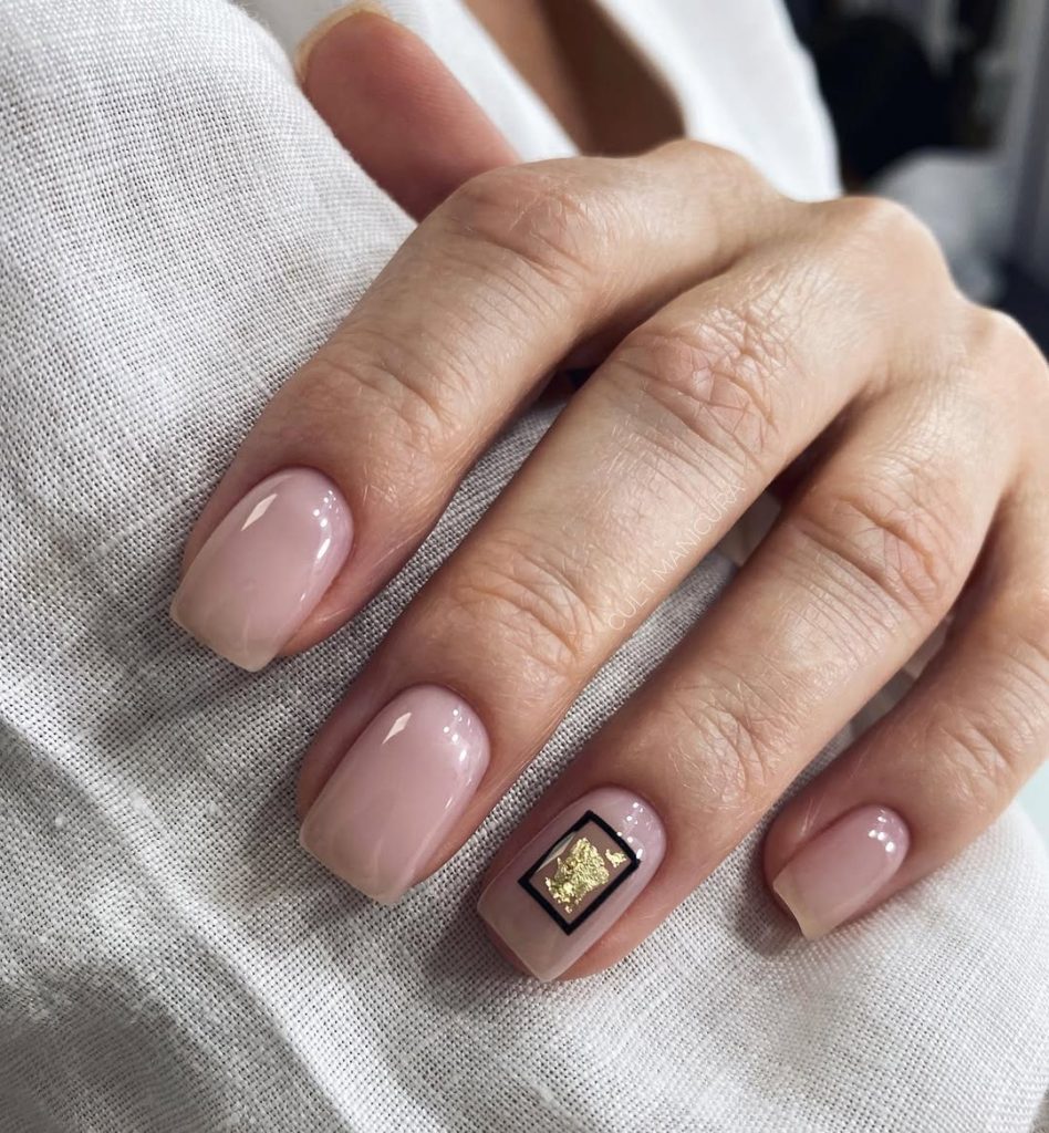 Short square minimalist nails with glossy milky nude polish and single gold foil accent framed in black on ring finger