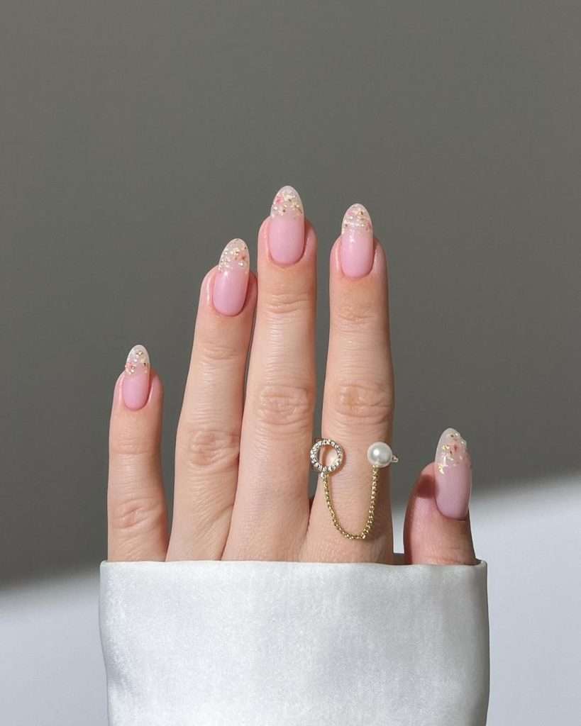 Almond shaped elegant pink nails with dried flower and pearl encrusted tips paired with pearl chain ring for luxury spring manicure