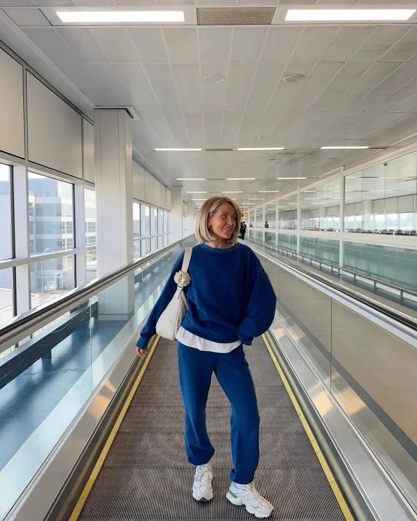 Comfortable airport outfit with navy blue sweatshirt, matching joggers, white layered t-shirt, chunky white sneakers and cream shoulder bag
