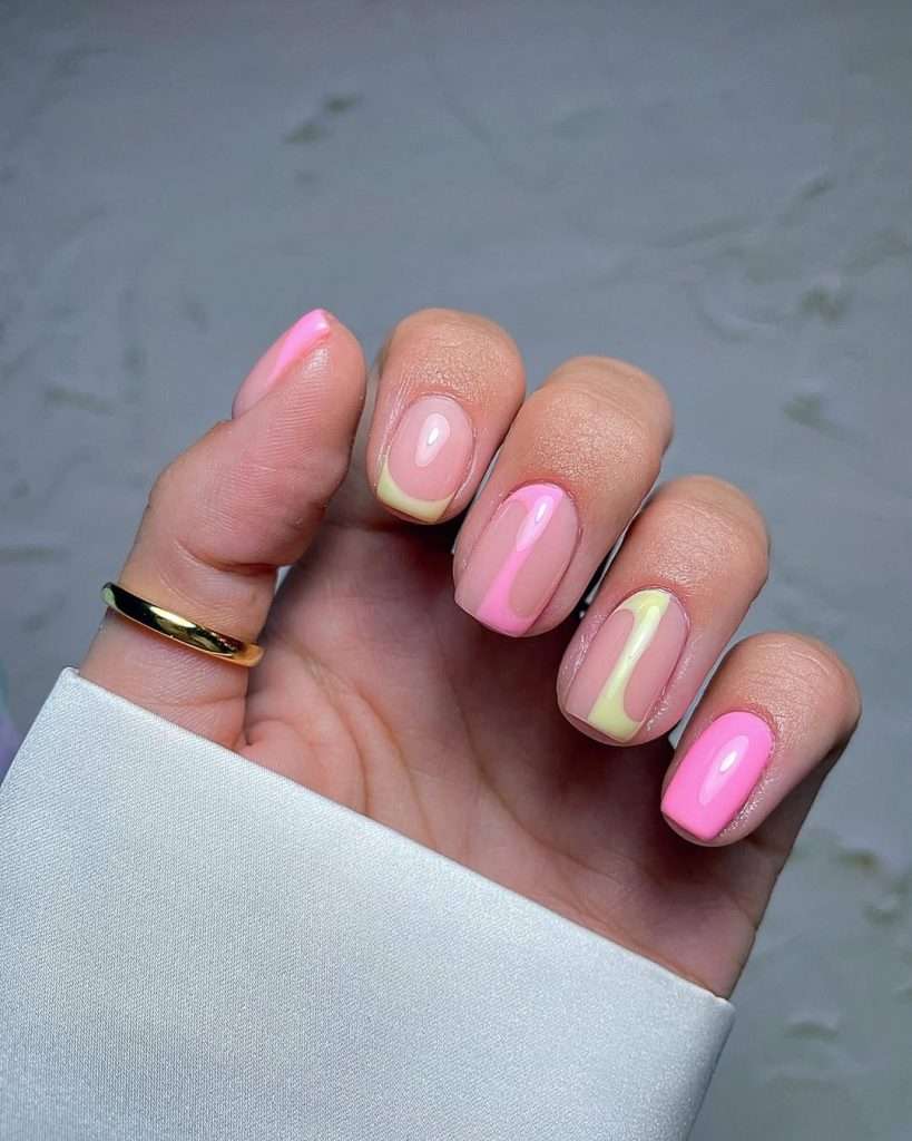 Short square nails with pink and yellow abstract swirls on nude base and one solid bright pink nail paired with gold ring for elegant spring manicure