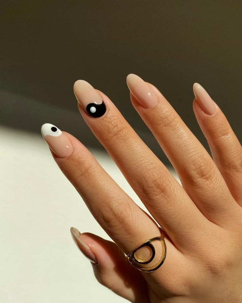 Almond-shaped minimalist nude nails with black and white yin-yang inspired art on two accent fingers