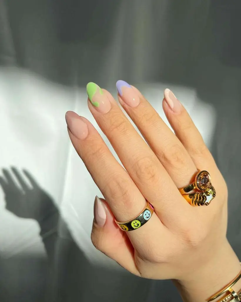 Almond shaped nude nails with abstract lime green and lavender accents paired with statement gold rings for elegant spring manicure