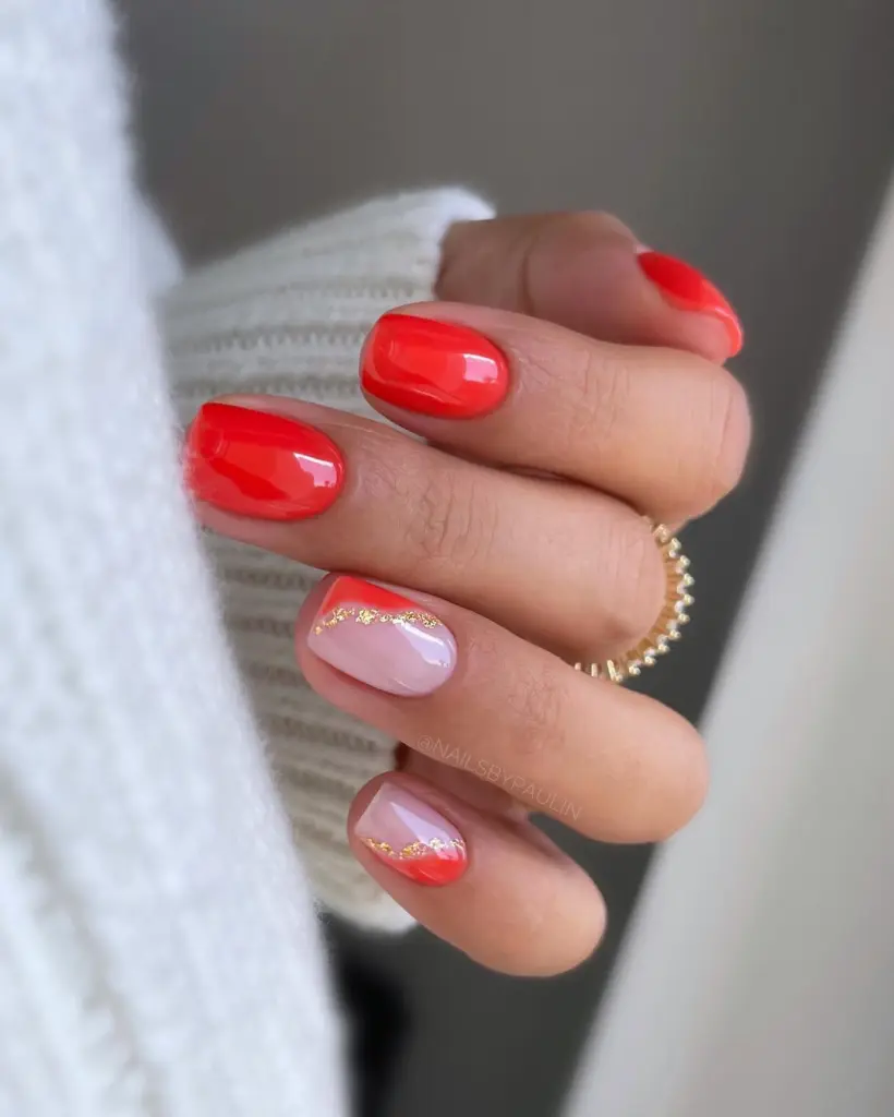 Short summer nails with bright coral red polish on most fingers and pink base with coral tips separated by gold glitter line on accent nails