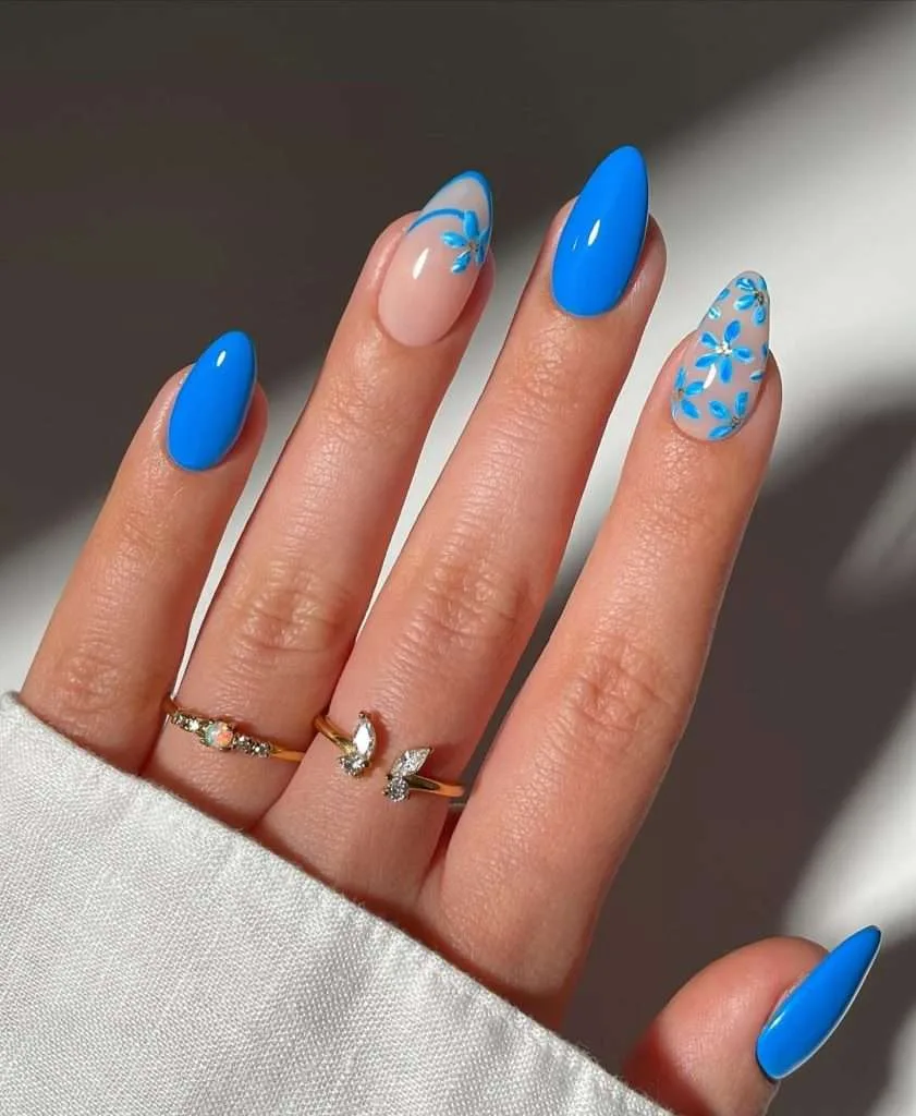Almond shaped spring nails with electric blue polish and sheer pink base with blue floral design