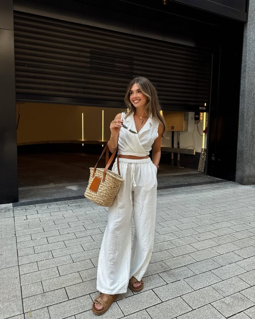 Elegant outfit with white wrap sleeveless top, white wide-leg linen pants, brown platform sandals and woven straw market tote