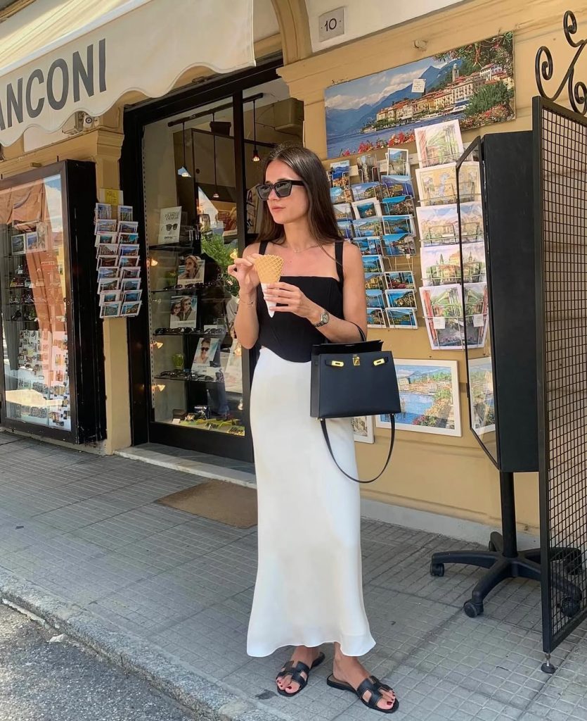 Classic European vacation outfit with black structured bustier top, white silk maxi skirt, black leather designer handbag and minimal sandals