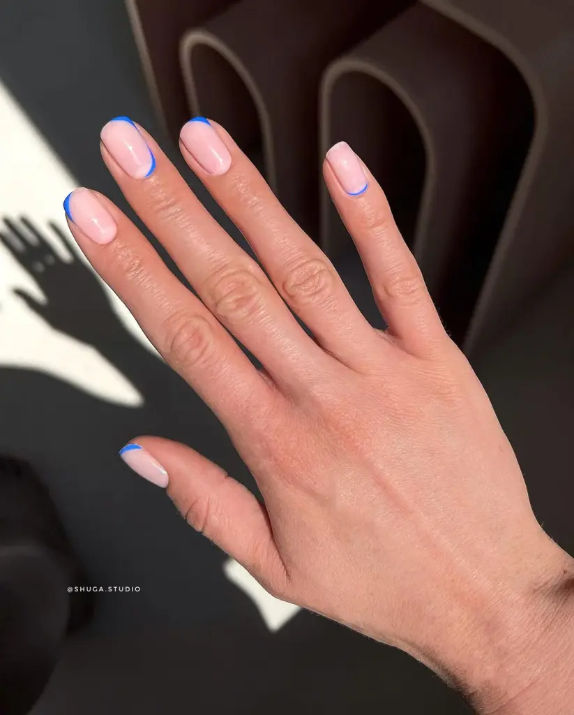 Short nails with pale pink base and thin electric blue outline accents positioned differently on each nail