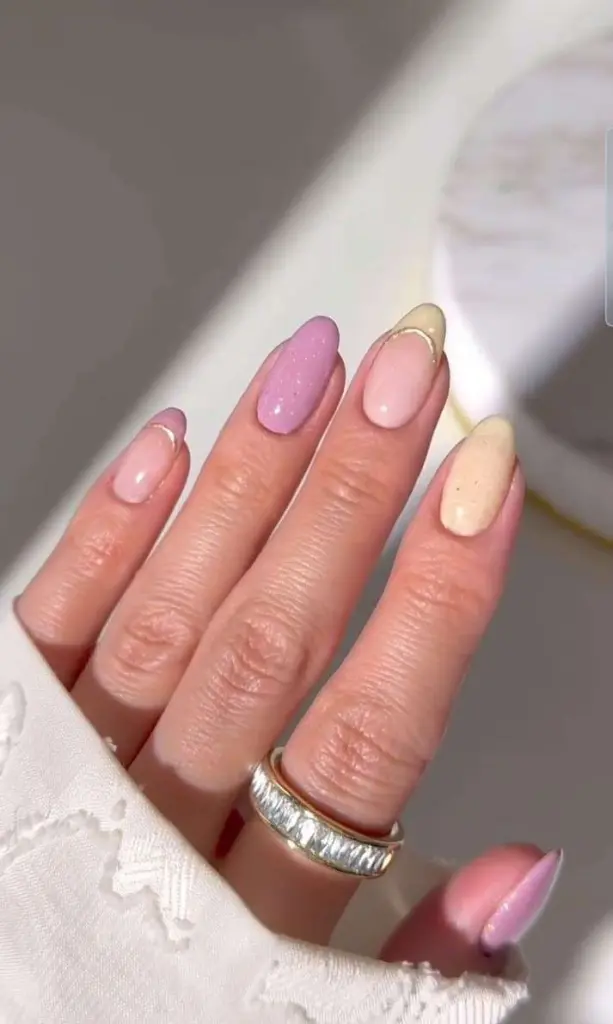 Almond shaped elegant nails with pastel pink, cream and lilac colors with gold French tips for classy spring manicure