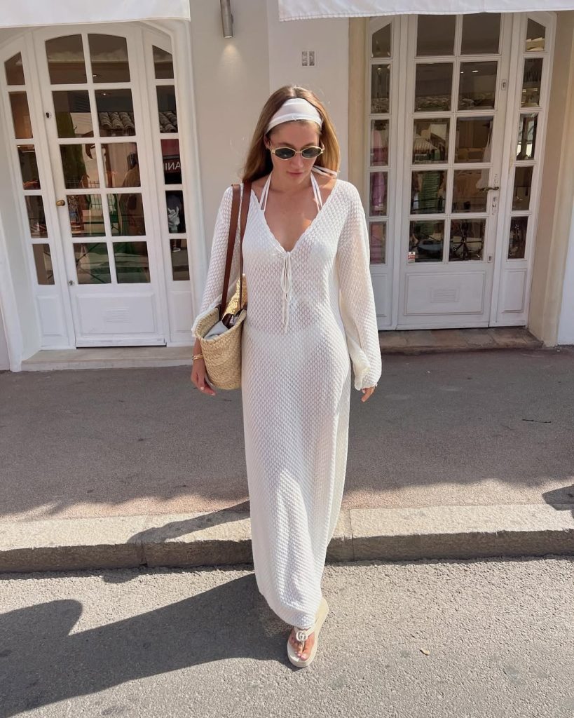Beach vacation outfit with white ribbed knit maxi dress featuring v-neck, long sleeves, straw tote bag, white headband and oval sunglasses