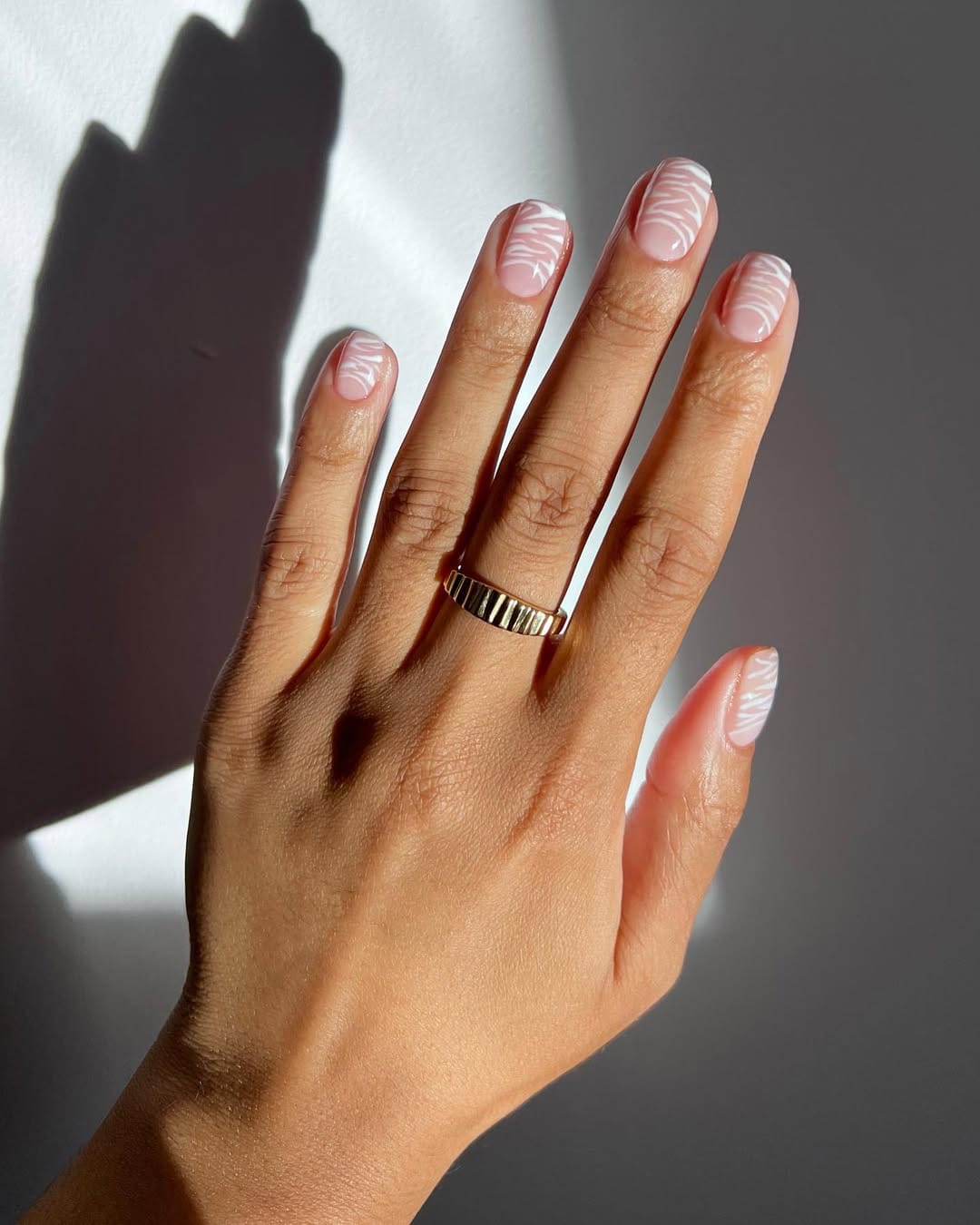 Short square minimalist nails with clear nude base and white abstract swirl pattern across each nail