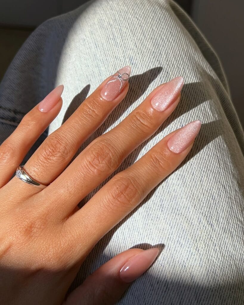 Almond minimalist nails with sheer pink shimmer and tiny wire bow detail on accent nail