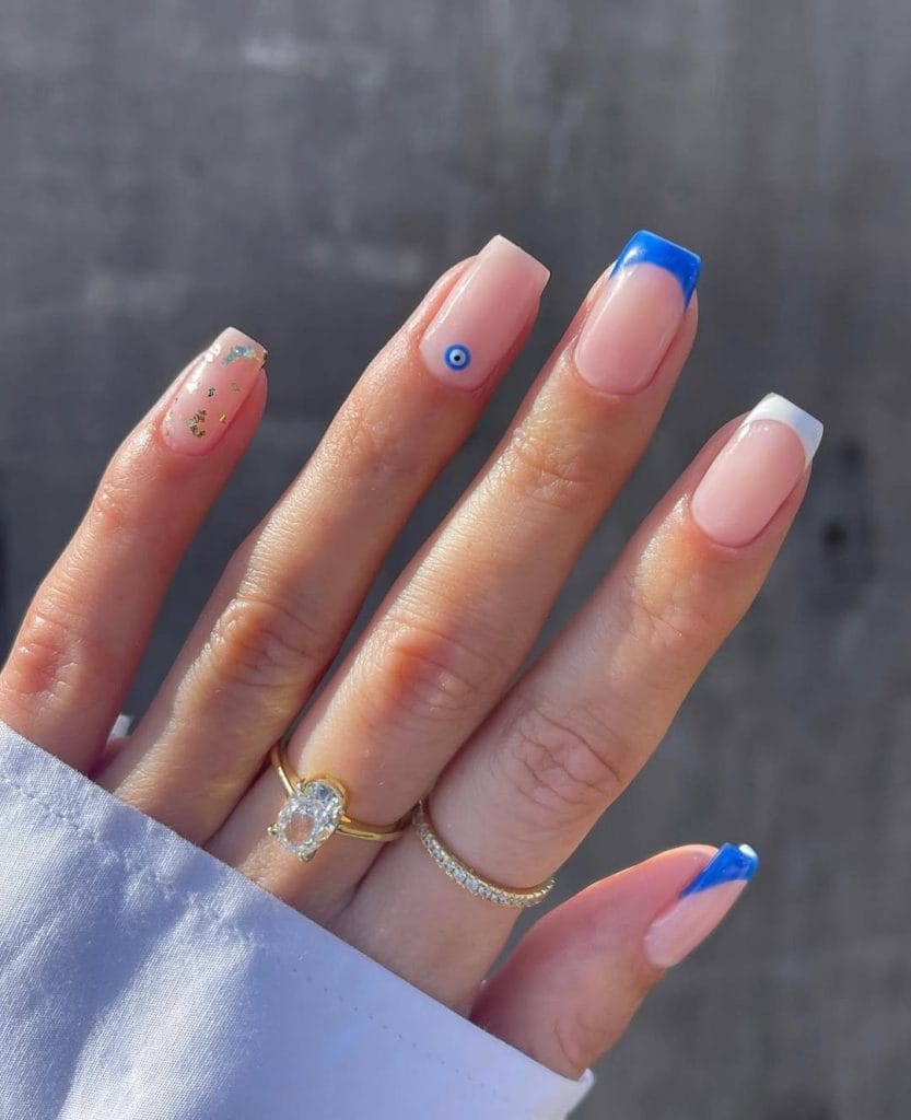 Long square vacation nails with blue and white French tips and evil eye charm accent on nude base
