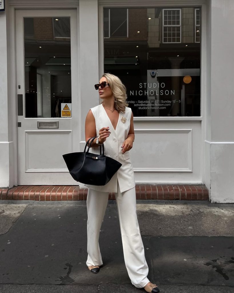 Elegant summer outfit with white sleeveless vest, matching wide-leg trousers, black structured tote bag, oversized sunglasses and two-tone ballet flats