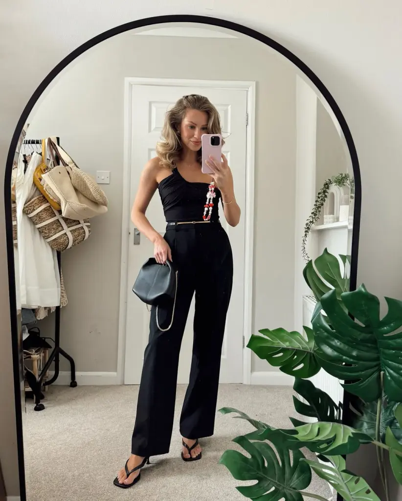 Sophisticated summer date night outfit with black asymmetric one-shoulder top, high-waisted wide-leg trousers, delicate gold belt and black thong heels
